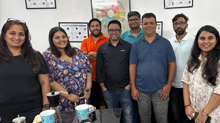 室内の、教育用ポスターの前で笑顔でポーズをとっている 3 人のチームメンバー。