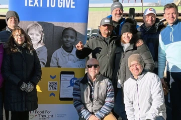 冬服を着たボランティアのチームが、地域のイベントで屋外で一緒にポーズをとっている。