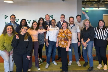 お祝いの旗で飾られたオフィススペースで、楽しそうにポーズをとっている同僚たち。